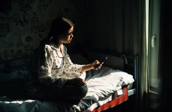 Portrait of a teenage girl with mobile phone sitting by the window in the village house. Concept of depression, loneliness, problems of adolescence